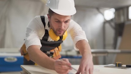 the working joiner draws a tape measure and a pencil on the material