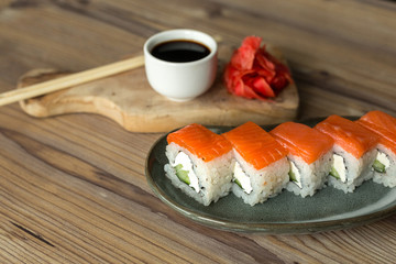 California sushi roll with salmon and cream cheese with ginger and soy sauce on a wooden table. Asian food with seafood