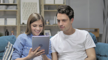 Young Couple Browsing Internet on Tablet while Relaxing on Couch