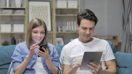 Young Couple Using Smartphone and Tablet while Relaxing on Couch