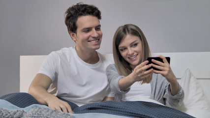 Couple Taking Selfie with Smartphone in Bed, Photograph