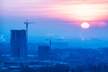 Tower cranes, the construction of a new tall apartment building at a construction site in the city at sunset or sunrise. Development, construction industry concept