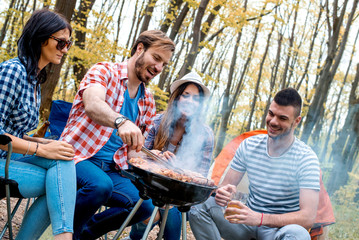 Group of friends making barbecue and having picnic in nature