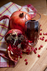 Fresh red pomegranate and glass of fresh rudy juice on a wooden background..