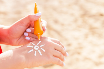 Young woman is applying sun cream on her hand in sun shape at the beach