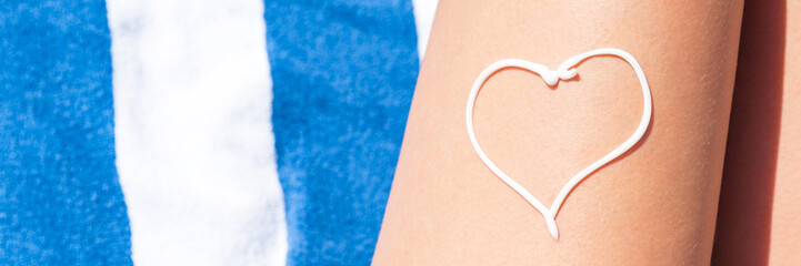 Sunscreen in the form of heart on woman's leg sunbathing on the towel by the sea