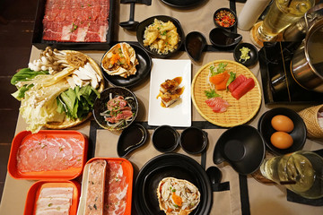 A table full of prepared plates of fresh vegetables, sliced Wagyu beef, pork meat, Sushi and Sashimi for Shabu Shabu (Japanese hot pot)