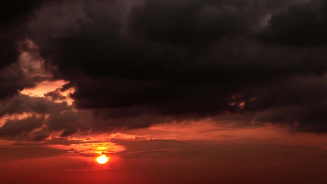 Time lapse of big orange sun setting down to the horizon on the red sky with gray dark clouds .4k footage.