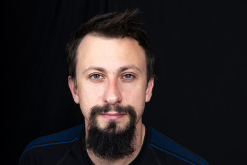 a close up portrait of a young man with beard in dark clothes on a dark background