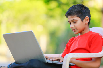 Cute little Indian/Asian boy studying or playing game with laptop computer