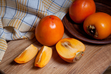 Whole ripe persimmon and sliced fruit on a wooden background..