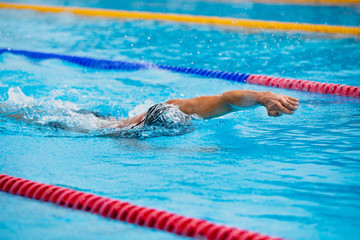 Athletic man swimming in front crawl style in the swimming pool with clear blue water.