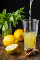 Top view of bottle serving lemon juice with lemons, mint and brown sugar, on dark wooden table in vertical