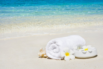 Fototapeta na wymiar White spa towel and flowers on sandy tropical sea beach
