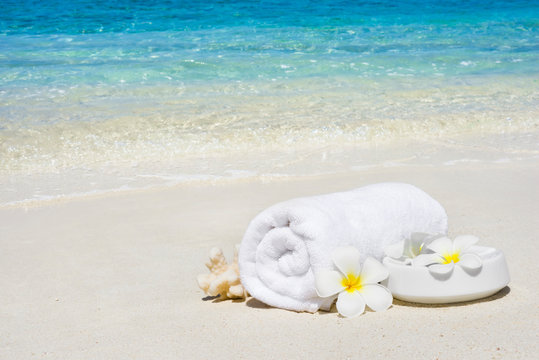 White spa towel and flowers on sandy tropical sea beach