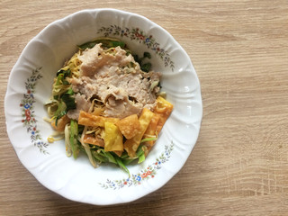 Dried egg noodles in a bowl mix topping with chopped pork, onion and fried wonton sheet, top view