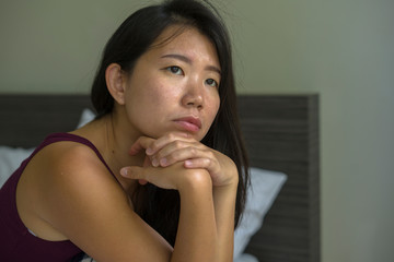 Fototapeta na wymiar lifestyle indoors portrait of young attractive sad and depressed Asian Korean woman at home sitting on bed emotional and thoughtful feeling worried and scared about life problem