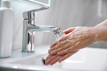 Young woman washing hands with soap over sink under faucet with water in bathroom. Girl doing...