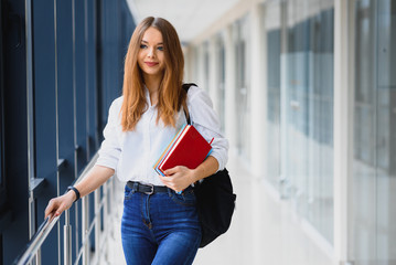 Positivity beautiful girl smiling at camera, standing on corridor with notes as backpack, going to lesson. Happy brunette female student studying in luxury university.
