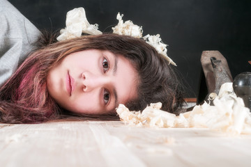 The face of a teenage girl lies on a planed board, a planer lies nearby and chips are lying. A strange abstract portrait.