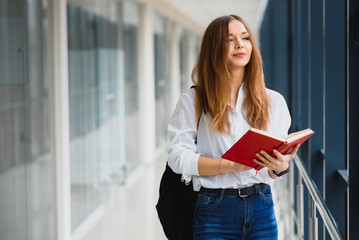 Cheerful brunette student girl with black backpack holds books in modern building. female student standing with books in college hallway