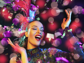 Surprised. Beautiful young woman in carnival, stylish masquerade costume with feathers on black background in neon light, flying confetti. Holidays celebration, dancing, fashion. Festive time, party. © master1305