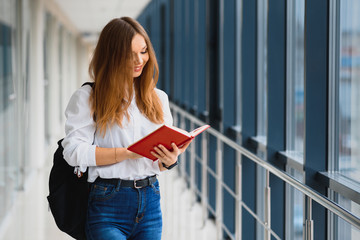 Positivity beautiful girl smiling at camera, standing on corridor with notes as backpack, going to lesson. Happy brunette female student studying in luxury university.