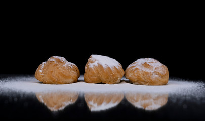 Profiteroles cakes in powdered sugar isolated on a black background.