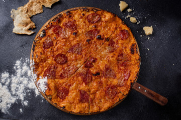 Italian pizza with salami and cheese on a thin cake on a board, black background.
