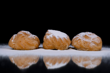 Profiteroles cakes in powdered sugar isolated on a black background, close-up.