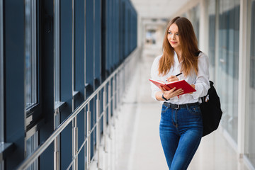 Positivity beautiful girl smiling at camera, standing on corridor with notes as backpack, going to lesson. Happy brunette female student studying in luxury university.