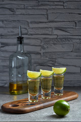 Three glasses of Golden tequila with lime slices, standing on a beautiful serving Board against a...