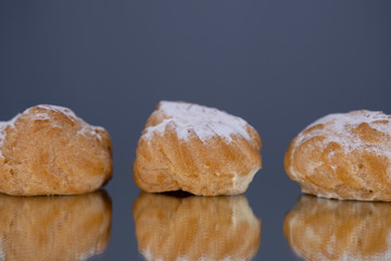 Profiteroles cakes on a reflecting surface isolated on a gray background, close-up.