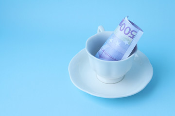 500 euros rolled up in a tube lies in a white coffee Cup. Coffee Cup with money. Tip. Crisis for cafes