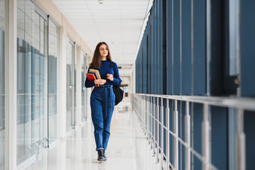 Portrait of a pretty female student with books and a backpack in the university hallway