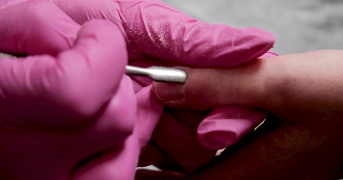 manicure master in pink gloves scraping off the old coat of varnish in manicure salon using drill.  Professional manicure in cosmetology clinic. Hygiene for hands in beauty salon. 