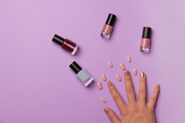woman hand with manicure and bottle with nail polish on purple backround