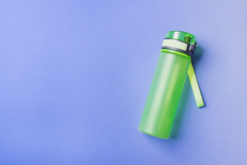green plastic sport bottle lying on right side of blue background with copy space