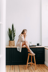 Morning breakfast, beautiful cute cute girl in home pajamas, dressing gown , making coffee sitting on the windowsill in a modern kitchen, weekend vacation, eco, freelance, comfort, spring