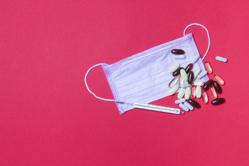 pink medical face mask, mercury thermometer and tablets on red background with copy space