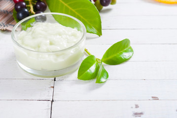 cosmetic cream in glass pot and leaves on white wood