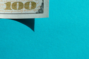 Piece of 100 dollar bill at the upper-left corner on the bright blue background. Conceptual photo, minimalistic design