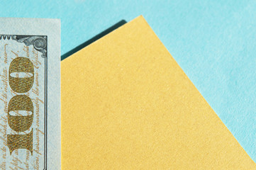 Piece of 100 dollar bill at the left corner on the golden yellow and blue background. Conceptual photo, minimalistic design