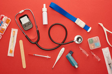 Top view of stethoscope, asthma inhaler, medicines and medical objects on red background