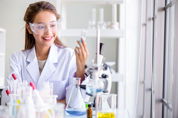 Attractive happiness Scientist woman using microscope testing some blood sample at laboratory with lab glassware on the table. Science or medical research and development new antivirus concept.