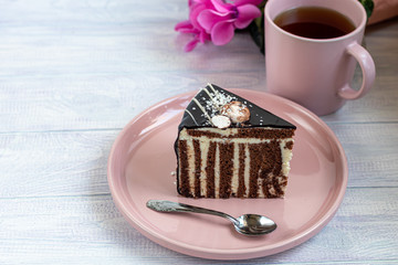 A slice of Zebra cake with chocolate icing. On a light background. In the background is a cup with floral tea.