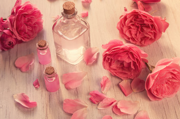 Rose water and oil in glass bottles with pink fresh rose flowers and petals on wooden background, SPA concept and aromatherapy