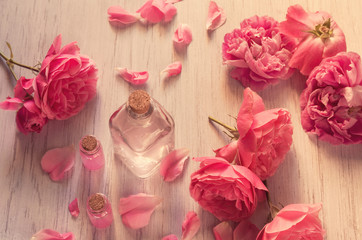 Beautiful still life with rose water in glass bottles and rose flowers on wooden table background, top view.