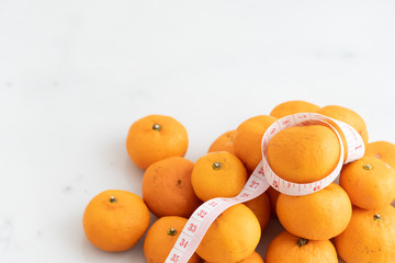 orange wrapped with measure tape  on white marble surface. Concept for fruit nutrition and diet food.