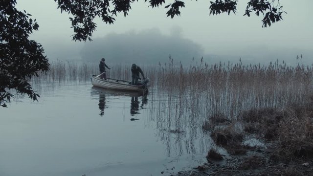 Father and son start up row boat and head through reeds among mist